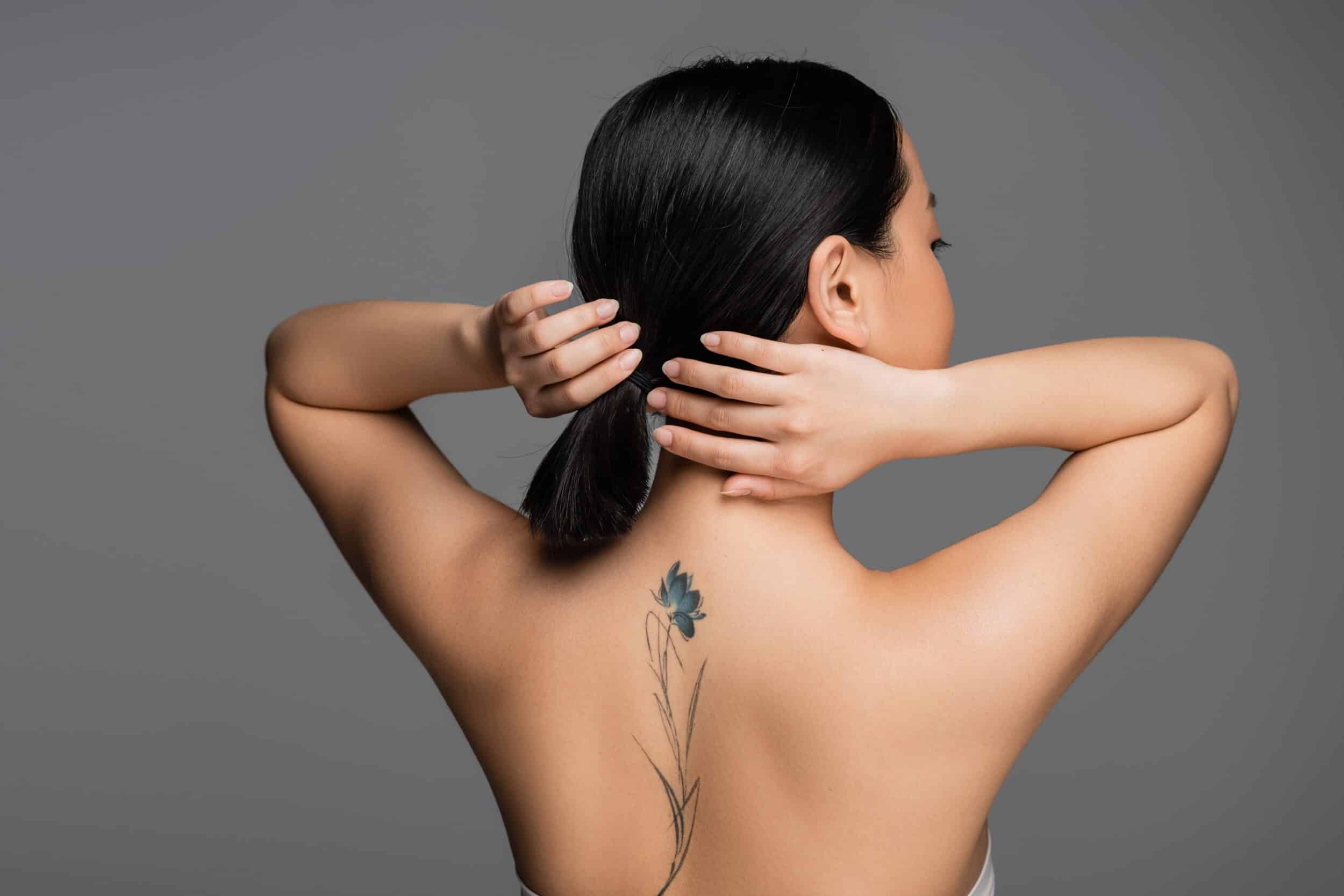 Brunette,Asian,Woman,With,Tattoo,On,Back,Touching,Ponytail,Isolated