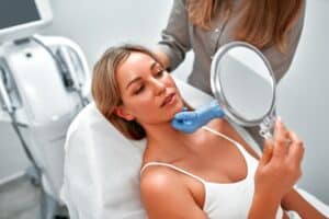 Woman examining her face in a mirror during a cosmetic consultation for fractional laser treatment