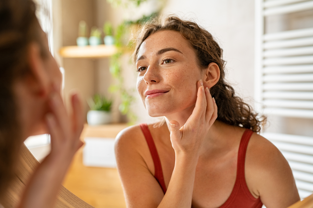 Woman examining uneven skin tone and facial pigmentation in mirror Woman examining uneven skin tone and facial pigmentation in mirror