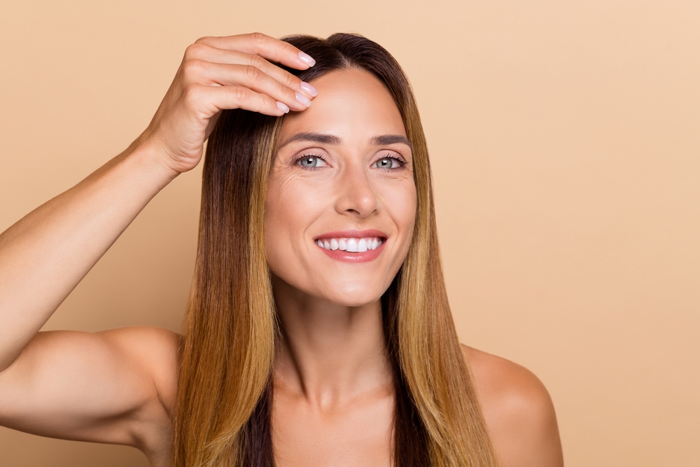 Woman smiling and touching her forehead to show calm, hydrated skin before an aesthetic treatment. Woman smiling and touching her forehead to show calm, hydrated skin before an aesthetic treatment.